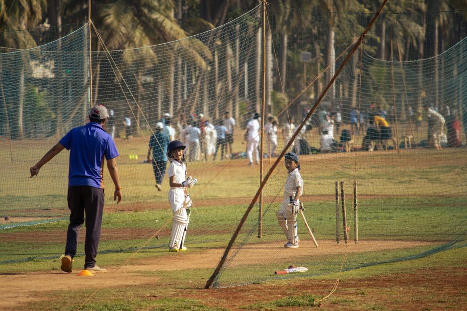 Young cricketers in whites at the practice nets with a coach