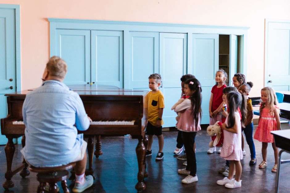 A music teacher at the piano with a group of young children